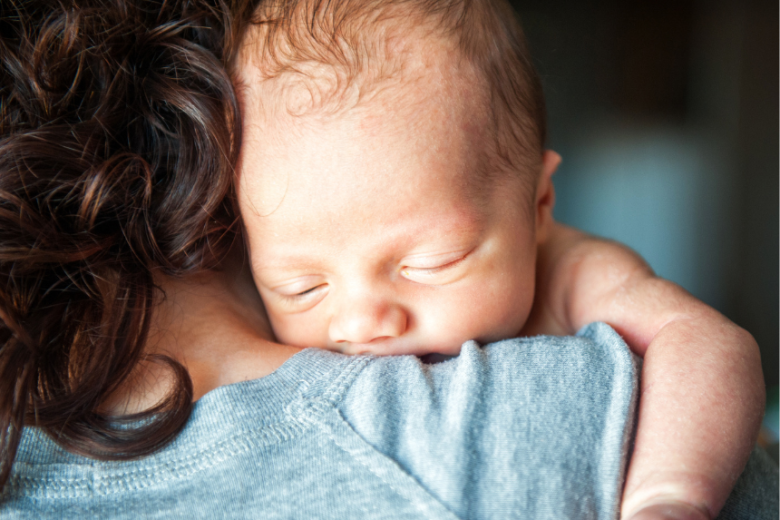 Parent and child foster carer cuddles sleeping baby into her shoulder