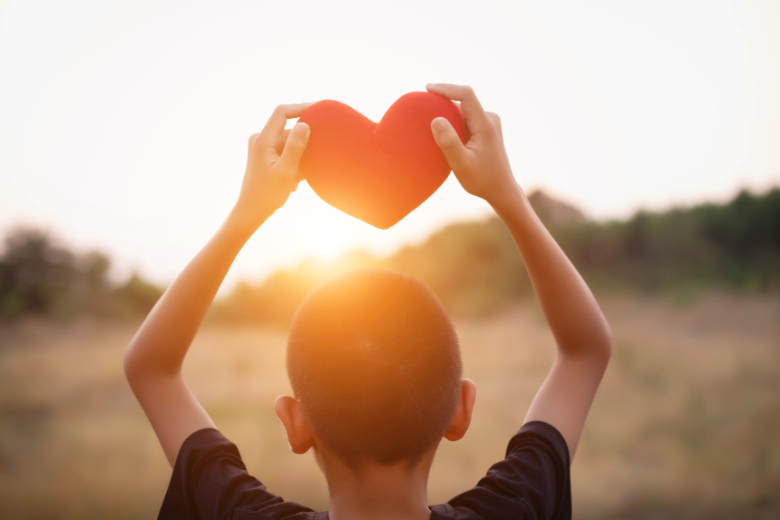 A boy holding a heart cutout above his head looking at the horizon - representing fostering and adoption support in the North West